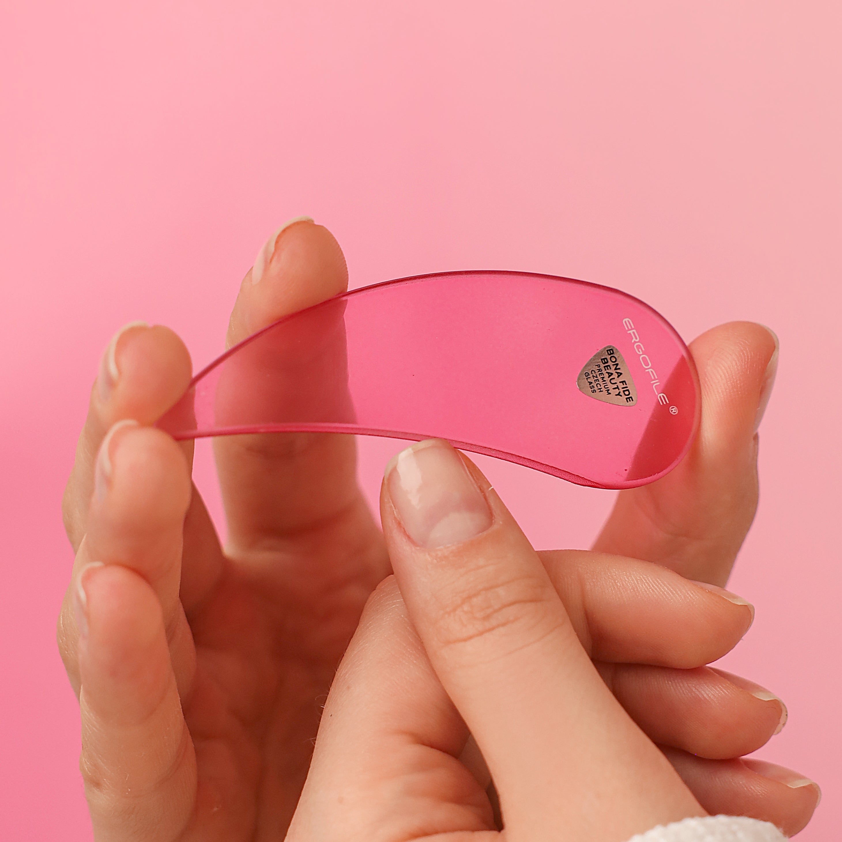 Hand holding a pink ergonomic glass nail file. Filing and shaping the corners of a thumbnail.